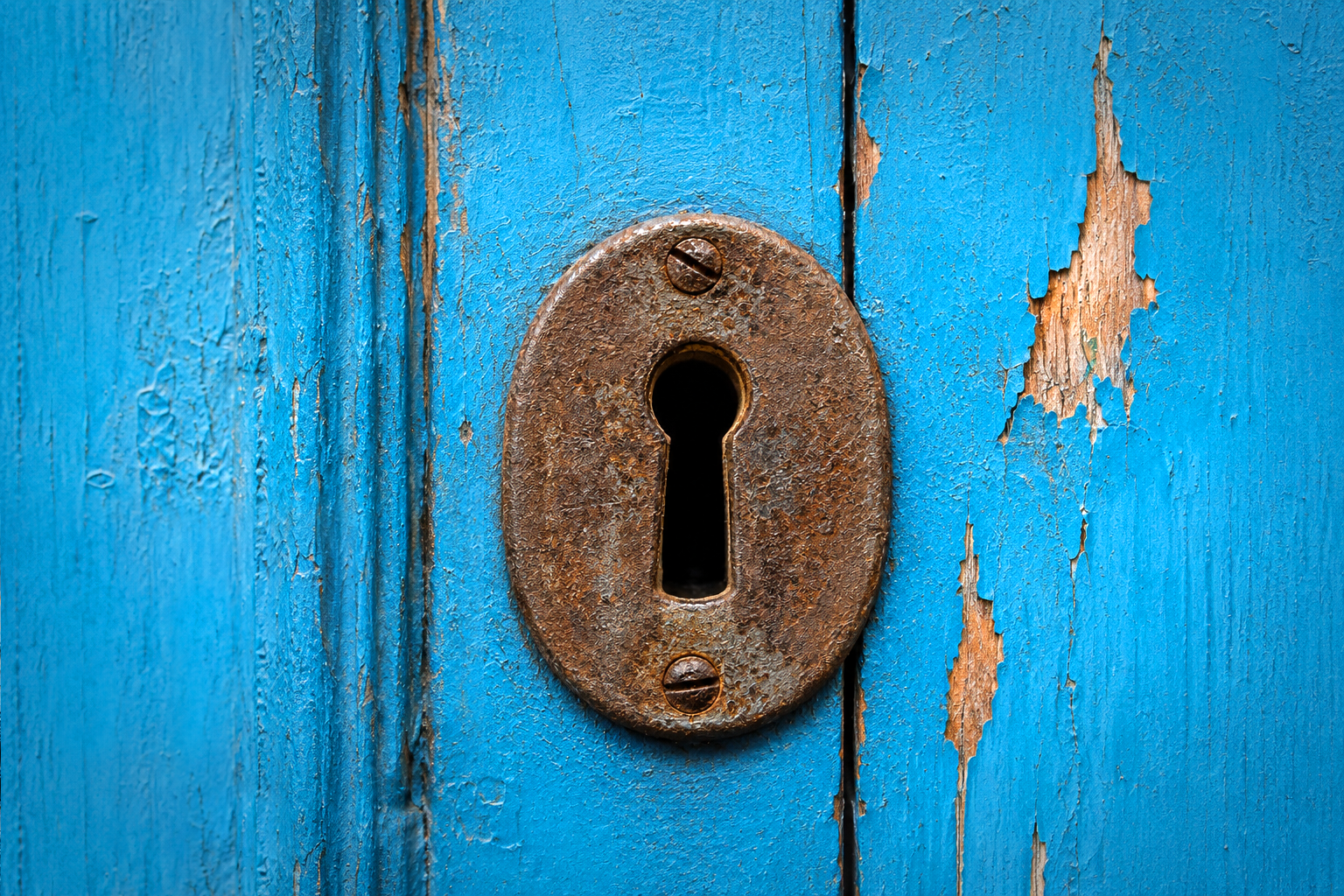 Rusty keyhole escutcheon in an old wooden door.